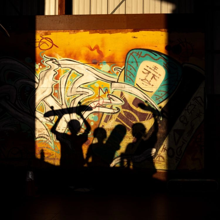 graffiti-covered wall with the shadows of people holding skateboards over their head